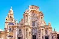 Intricate Baroque architecture of the Cathedral of Murcia against a clear blue sky.